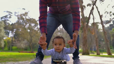 Boy-lying-on-skateboard,-rolling-to-camera-with-help-of-father